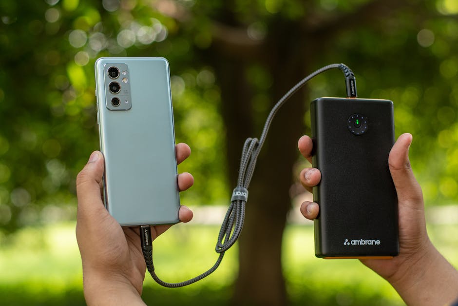 Close de mãos segurando um smartphone conectado a um power bank ao ar livre.