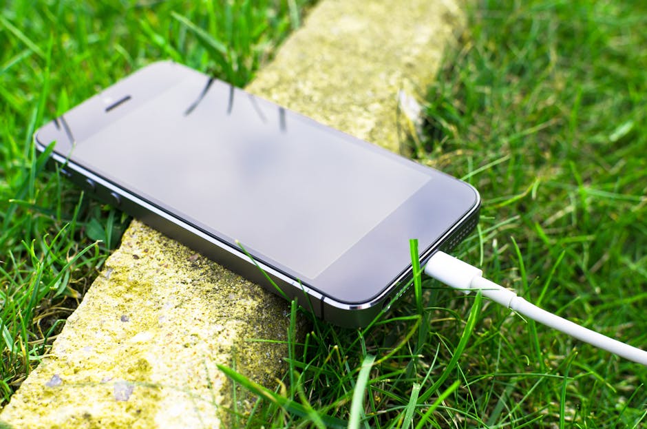 Um smartphone com um cabo de carregamento repousa na grama ao ar livre, apresentando a tecnologia moderna na natureza.