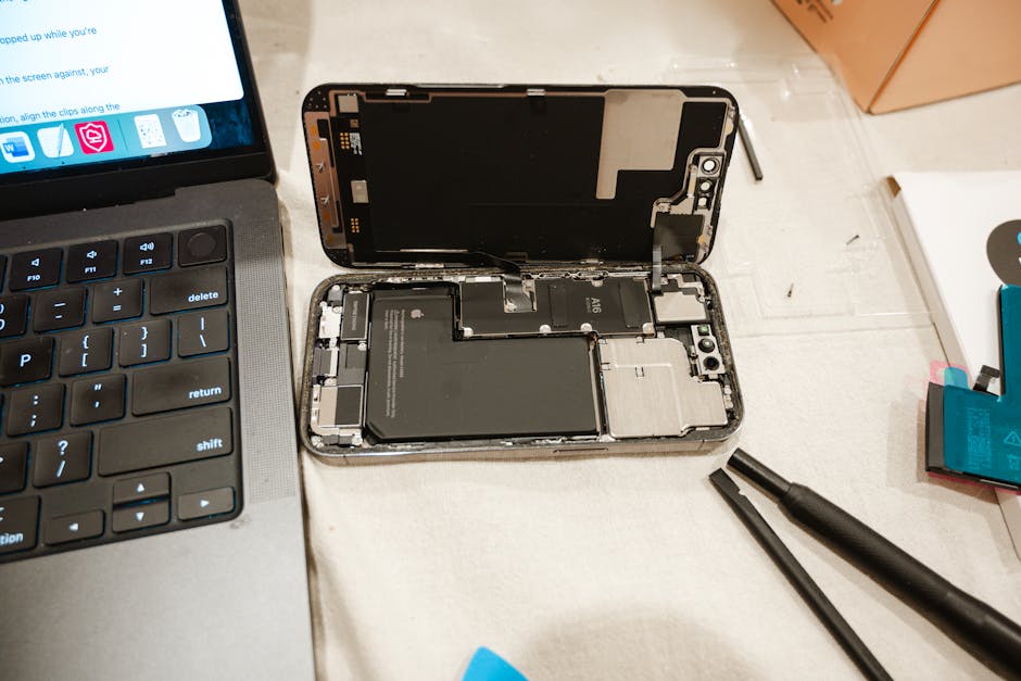 Abra o iPhone com ferramentas de reparo e laptop, apresentando o processo de substituição de bateria DIY.