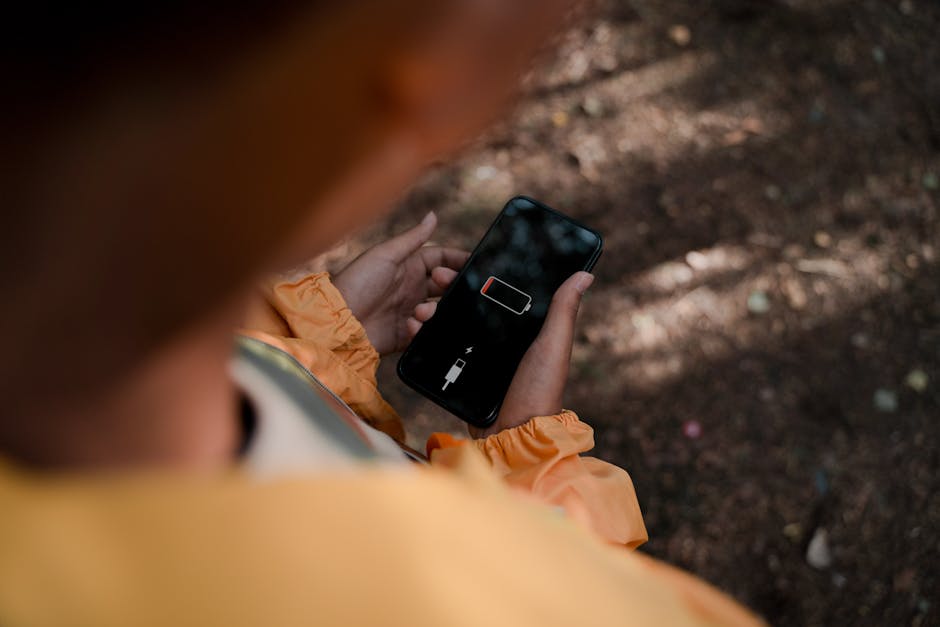 Adolescente segura um smartphone exibindo bateria fraca ao ar livre em uma floresta.