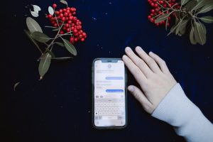 Uma mão ao lado de um smartphone mostrando uma conversa por mensagem de texto, cercada por bagas vermelhas.
