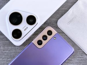 Close de dois smartphones com foco na câmera em uma superfície de madeira texturizada.